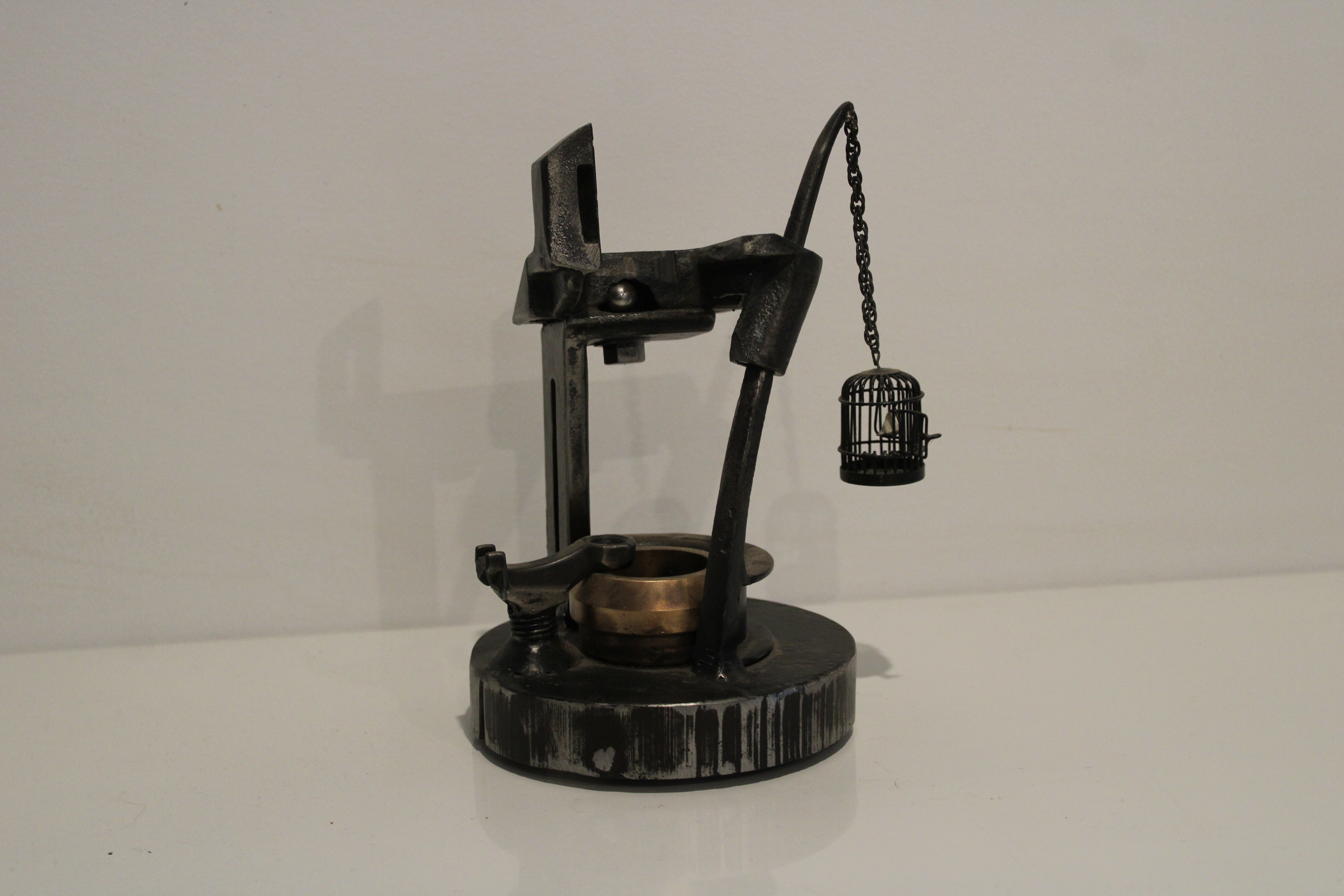 An abstract steel and brass sculpture of a well and bird cage