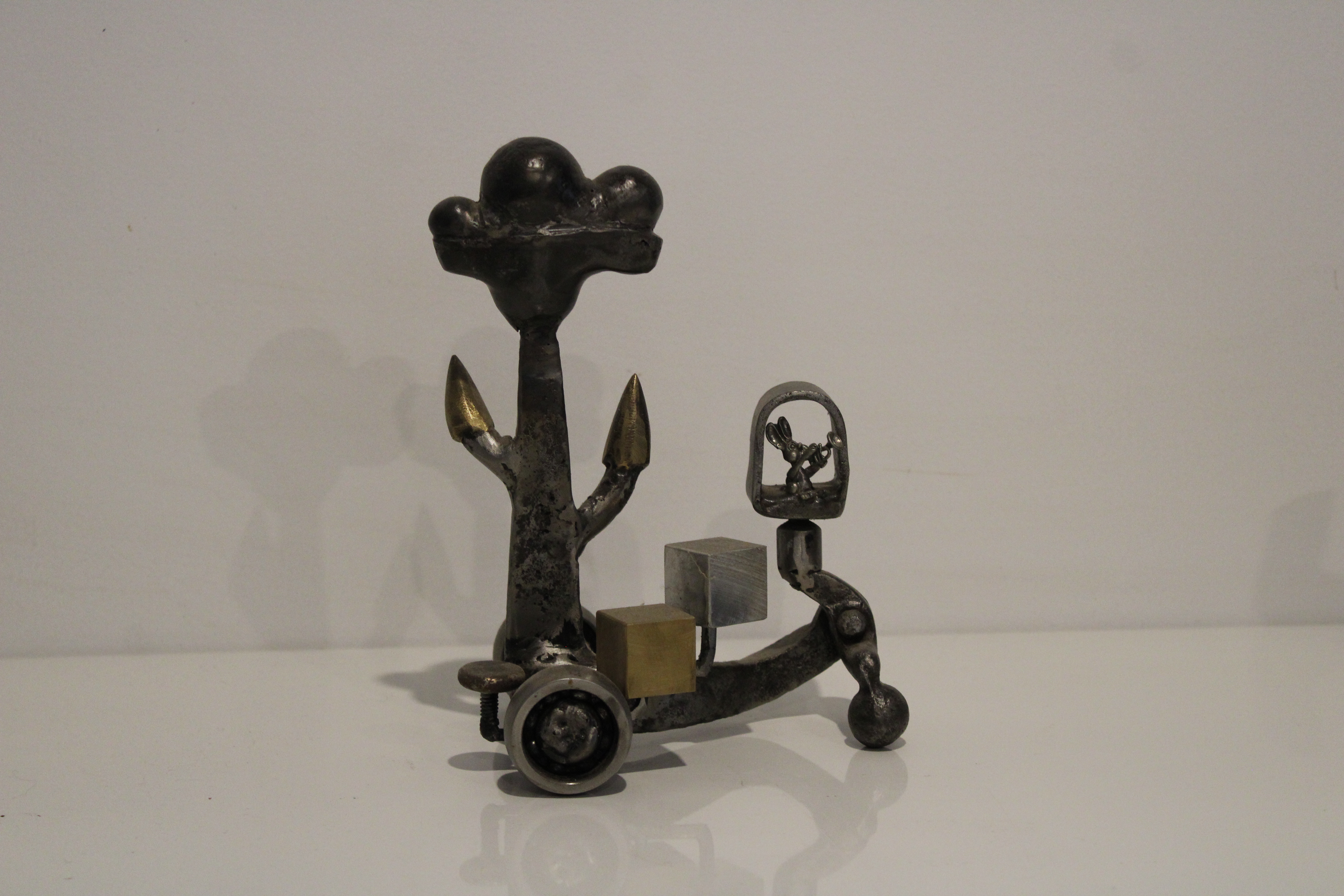 An abstract steel and brass sculpture depicting a rabbit on a tricycle with a tree